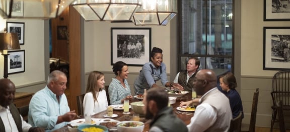 A server delivers a large plate of food to smiling dinner guests at a large banquet table.