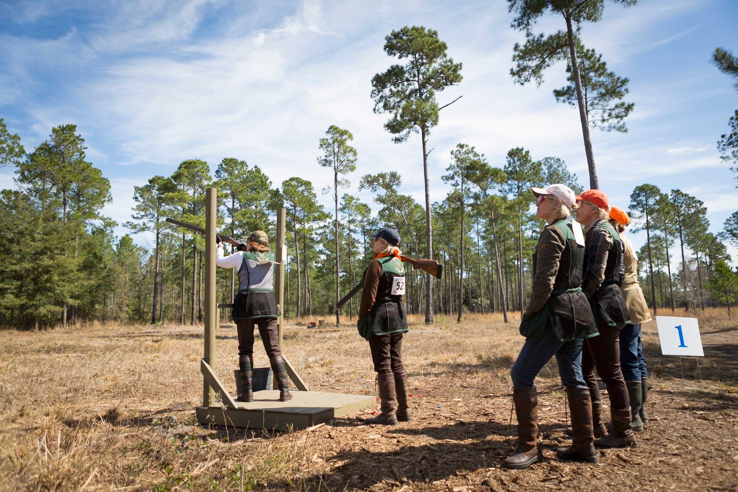 A woman shoots during a competition while a small group watches on a sunny day.