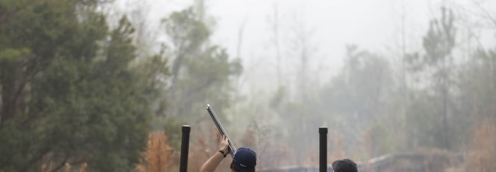 A man shoots a long gun on a foggy day during a Seminole Cup competition while a judge watches next to him.