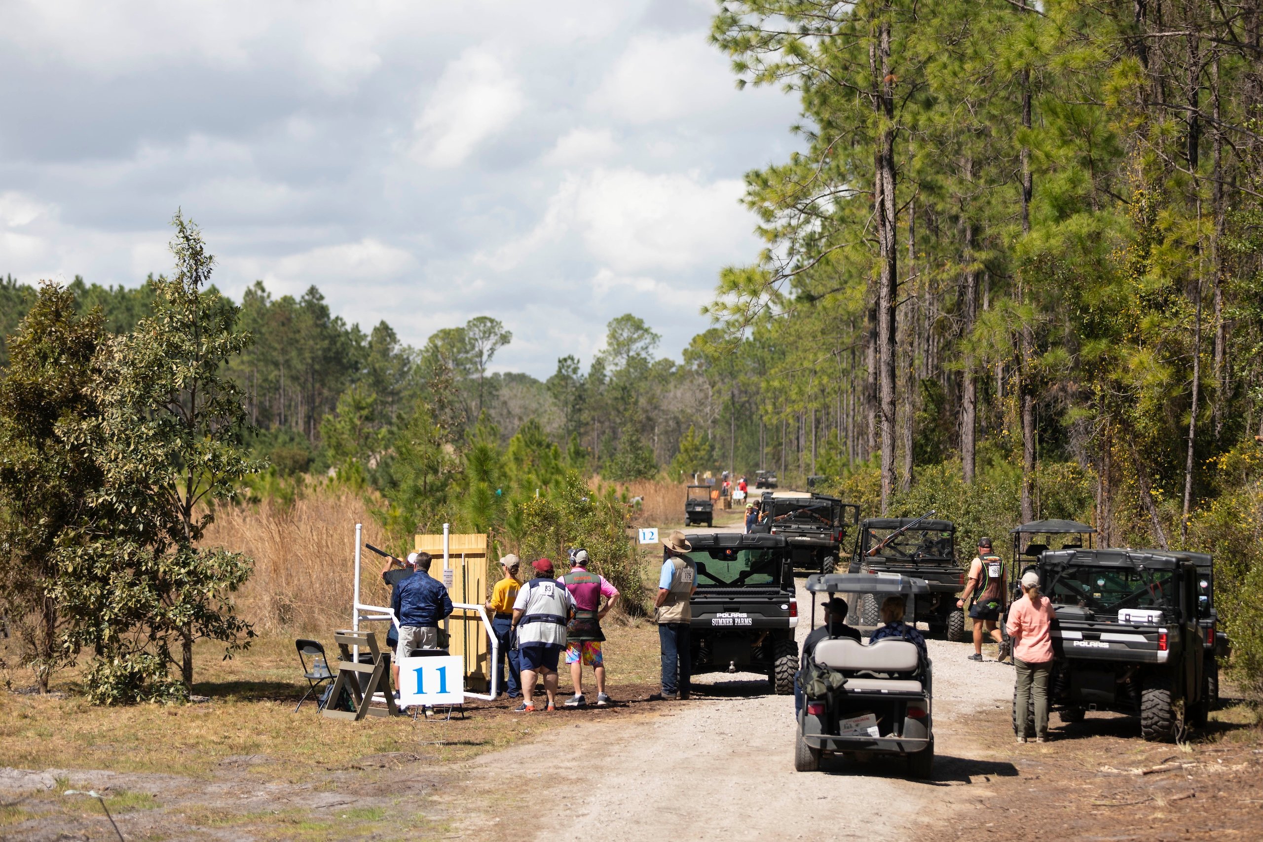 View of a Seminole Cup competition area on a field on sunny day. There are groups of competitors set up with a line of golf carts behind them.