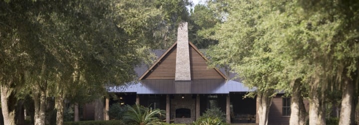 The Broadfield Lodge, a large modern cabin with mature trees on either side of the drive way.