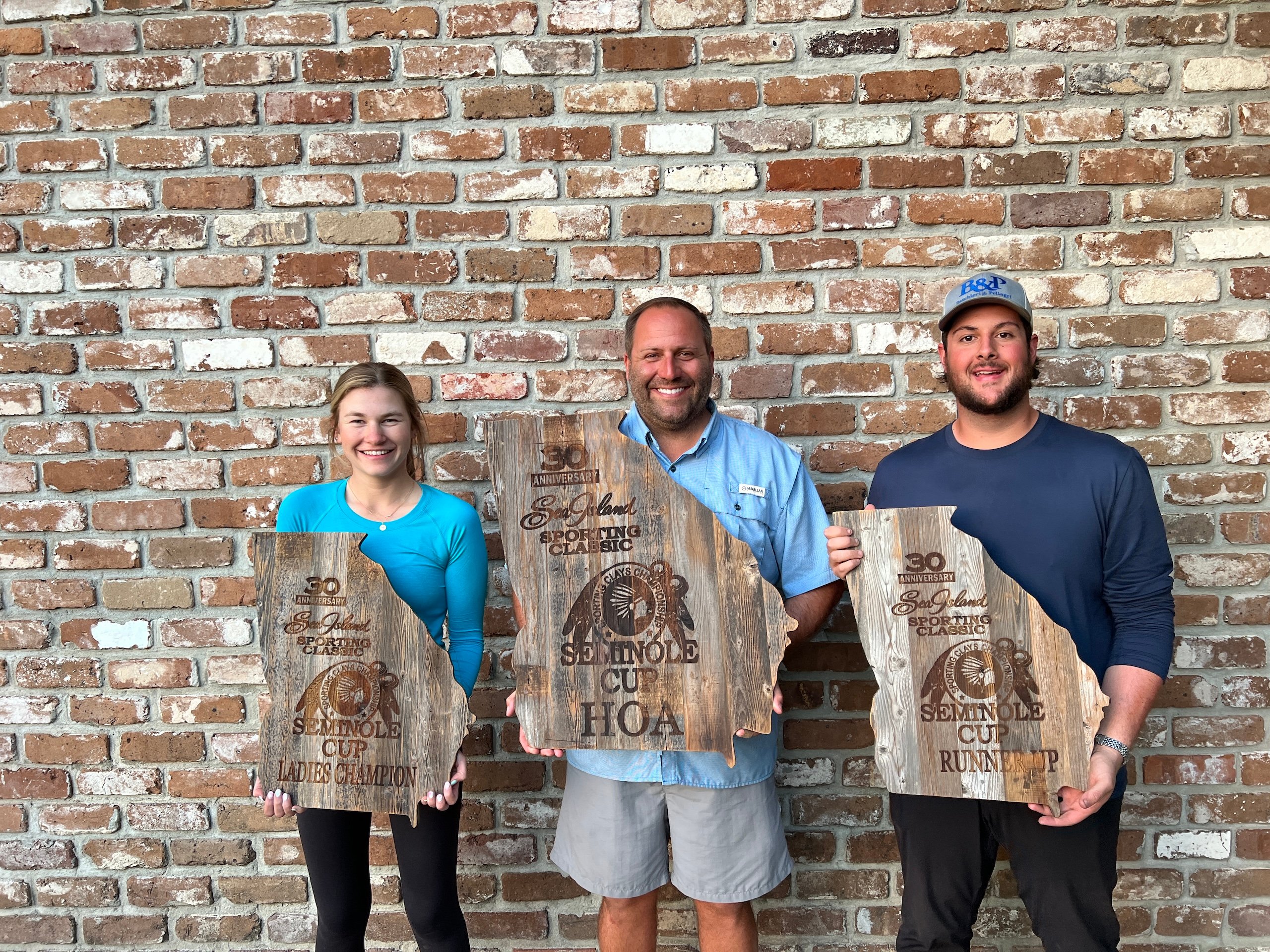 A girl and two men from a Seminole Cup competition hold up their awards - wooden planks cut in the shape of Georgia.