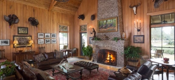 The rustic interior of a cottage with large stone fireplace, leather furniture and taxidermied animals hung on the walls.