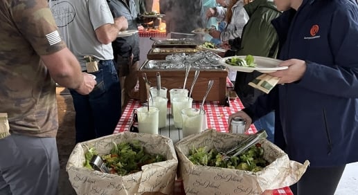 People partaking in a banquet of salads and assorted barbecue dishes.