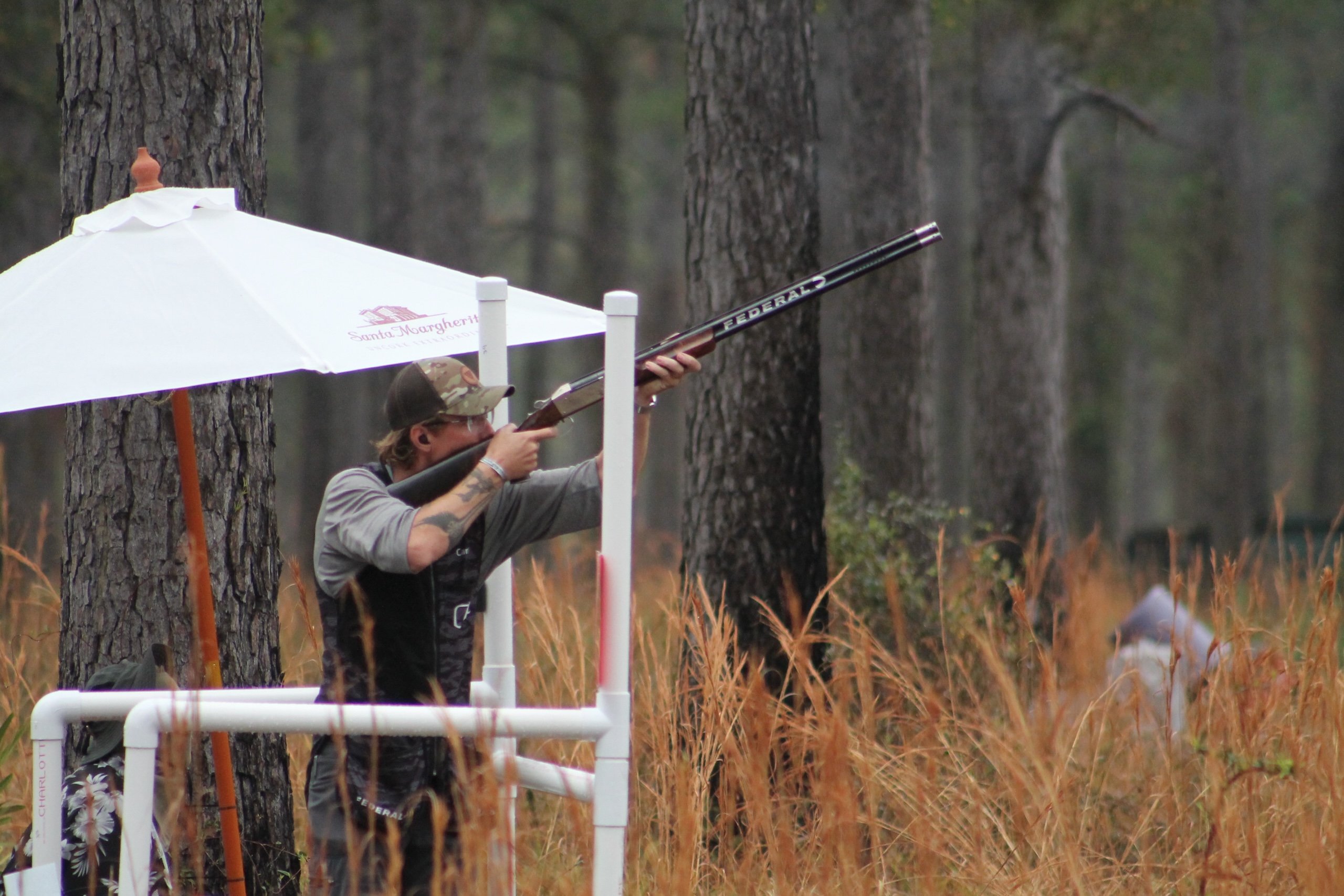 A man in a baseball cap aims a long gun during a shooting competion.